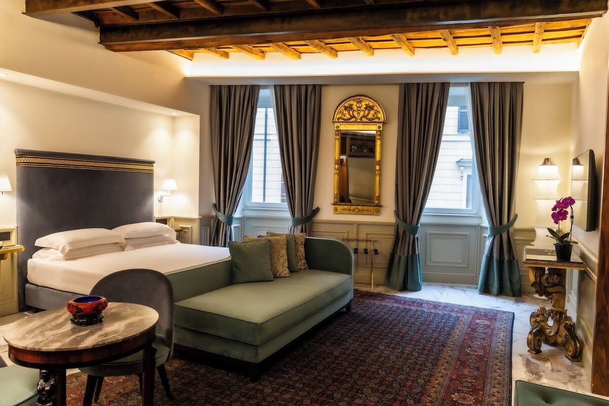 Une chambre d’hôtel comprenant un lit, un canapé, une petite table, un miroir et une plante décorative.