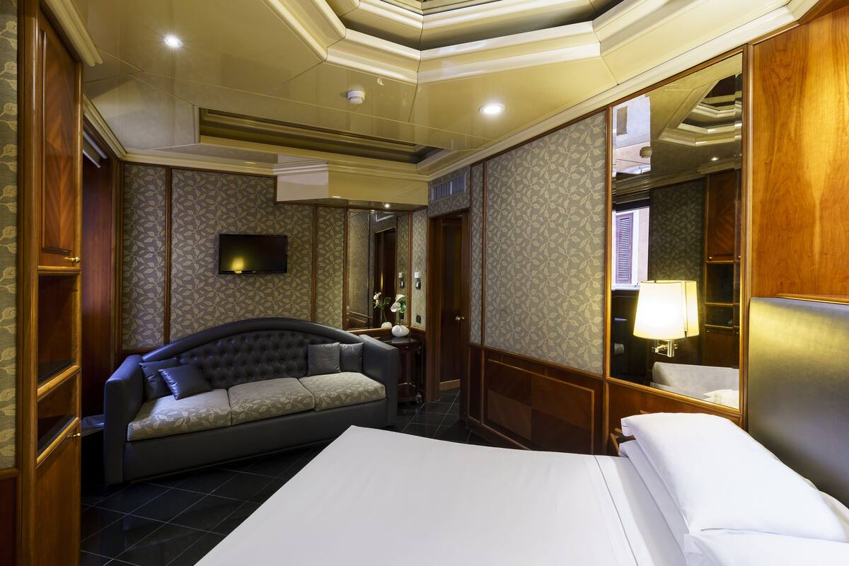 Une chambre d’hôtel avec un lit, un canapé, une télévision et un miroir.
