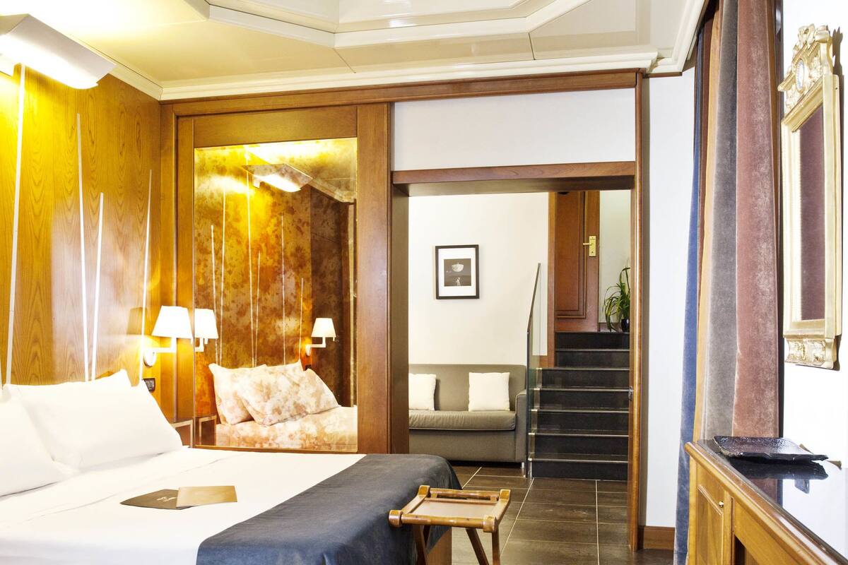 Une chambre d’hôtel avec un grand lit, un bureau, une chaise, un canapé et un escalier menant à un autre étage.