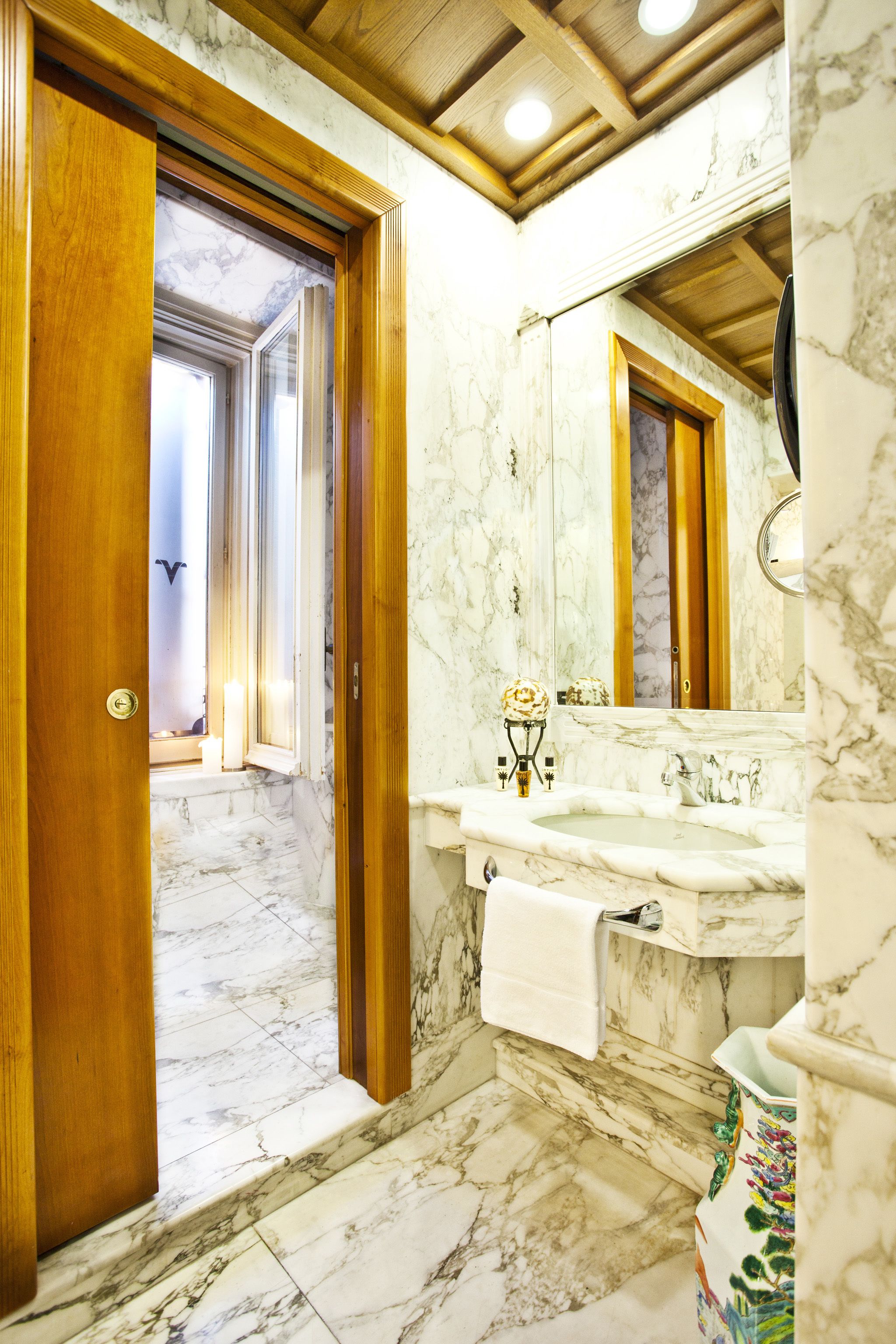 A bathroom with marble flooring, a wooden door, a sink with a mirror, and a towel hanging on the wall.