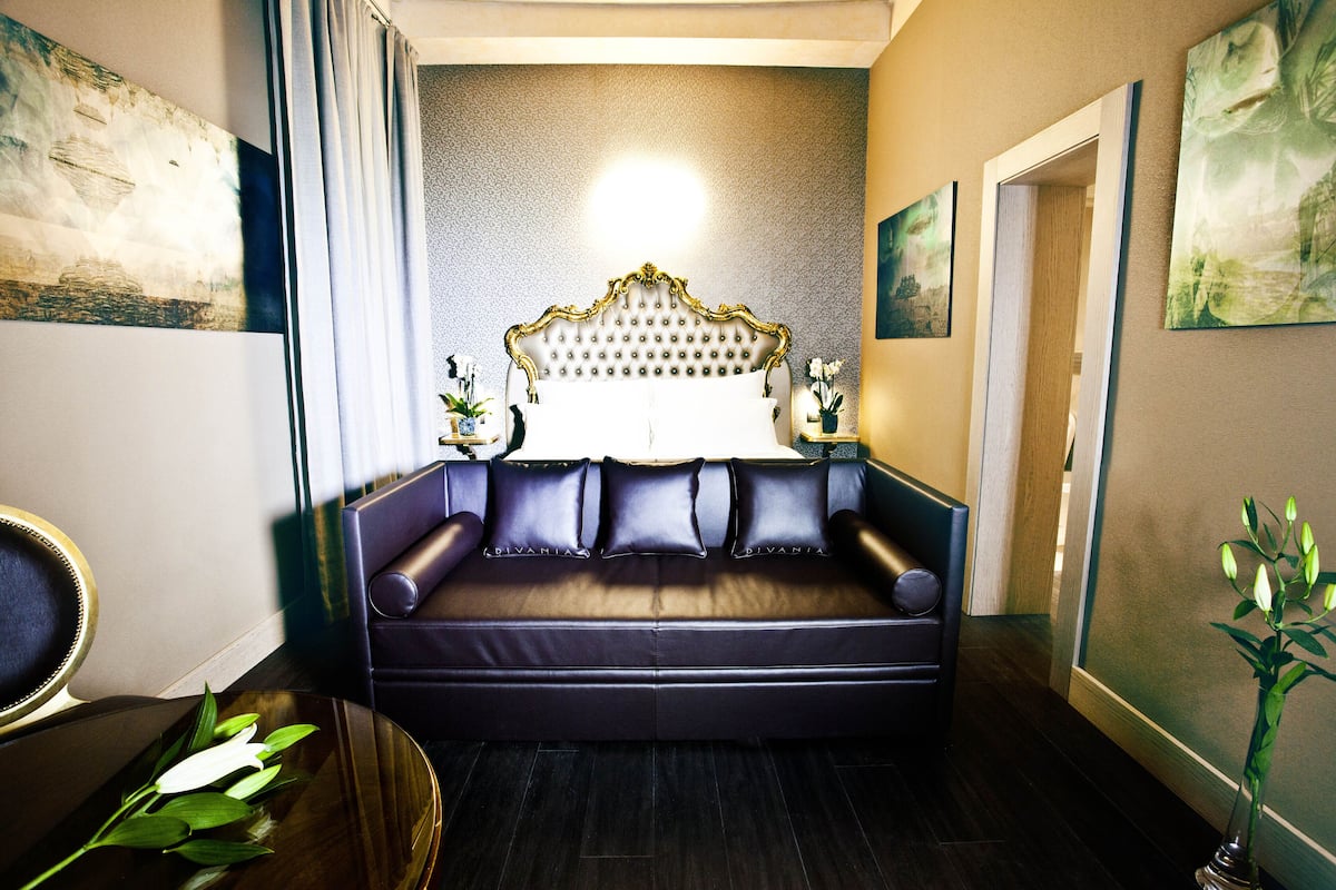 Un canapé de couleur sombre, doté d’un haut dossier capitonné, se trouve dans une pièce dont le mur présente une texture particulière et qui est décorée d’œuvres d’art.