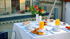 Une table dressée pour le petit-déjeuner, avec des viennoiseries, des fruits et du jus, donnant sur un quartier résidentiel avec des maisons et de la verdure.