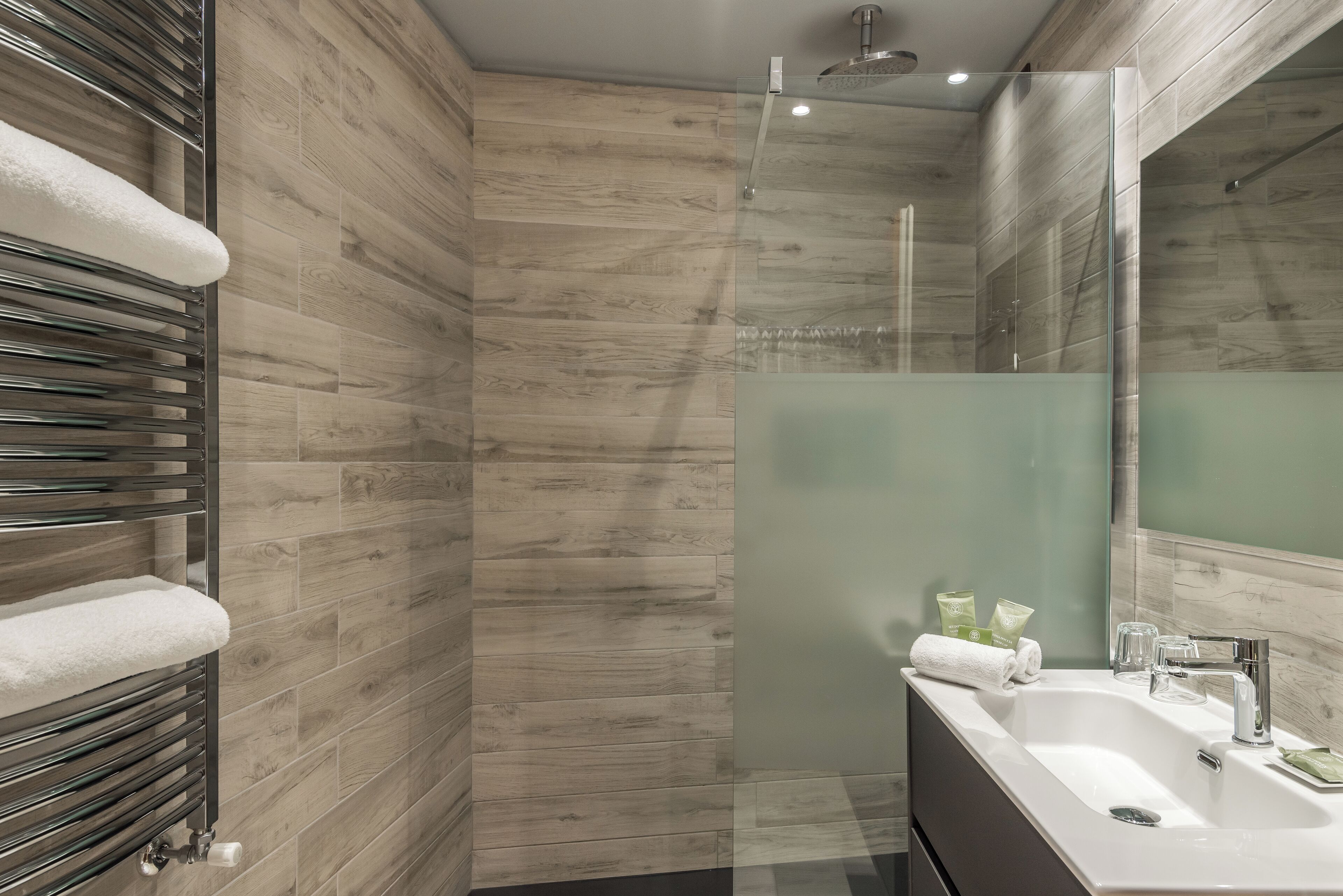 A modern bathroom with a glass shower enclosure, a built-in sink with a mirror, and a towel rack with a white towel.