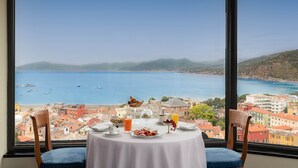 Mesa posta para o café da manhã, com vista panorâmica do mar e edifícios.