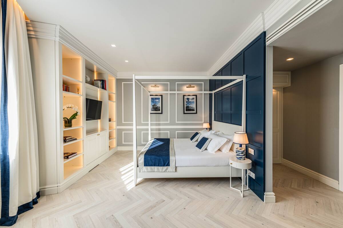 A bedroom with a bed, bedside tables, a wardrobe, and built-in shelving with books and decorative items.