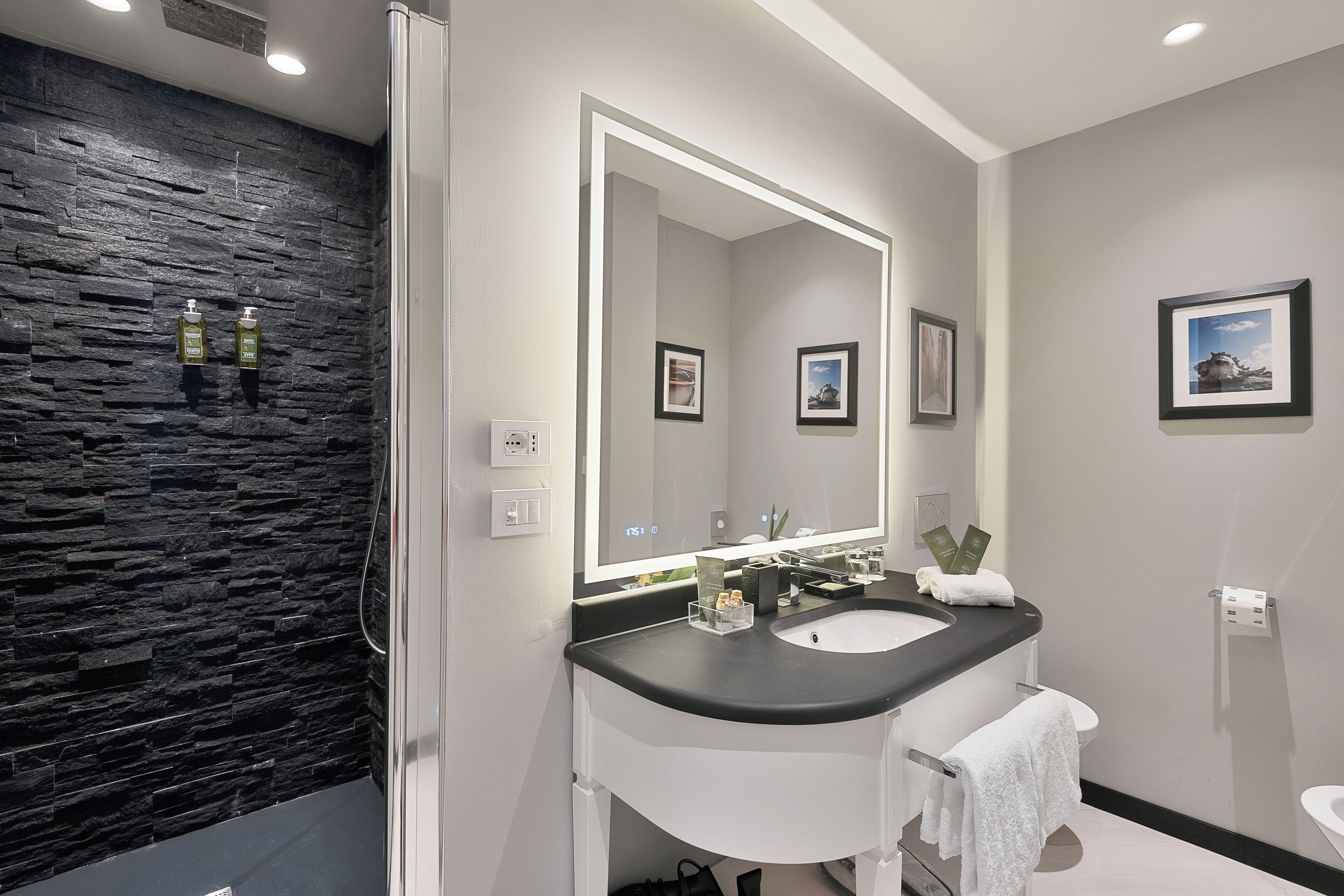 A modern bathroom with a stone wall, a large mirror, a white sink, and a toilet.
