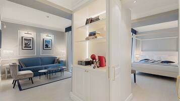 A modern living room with a blue sofa, a white cabinet with shelves, and a bed with white bedding.