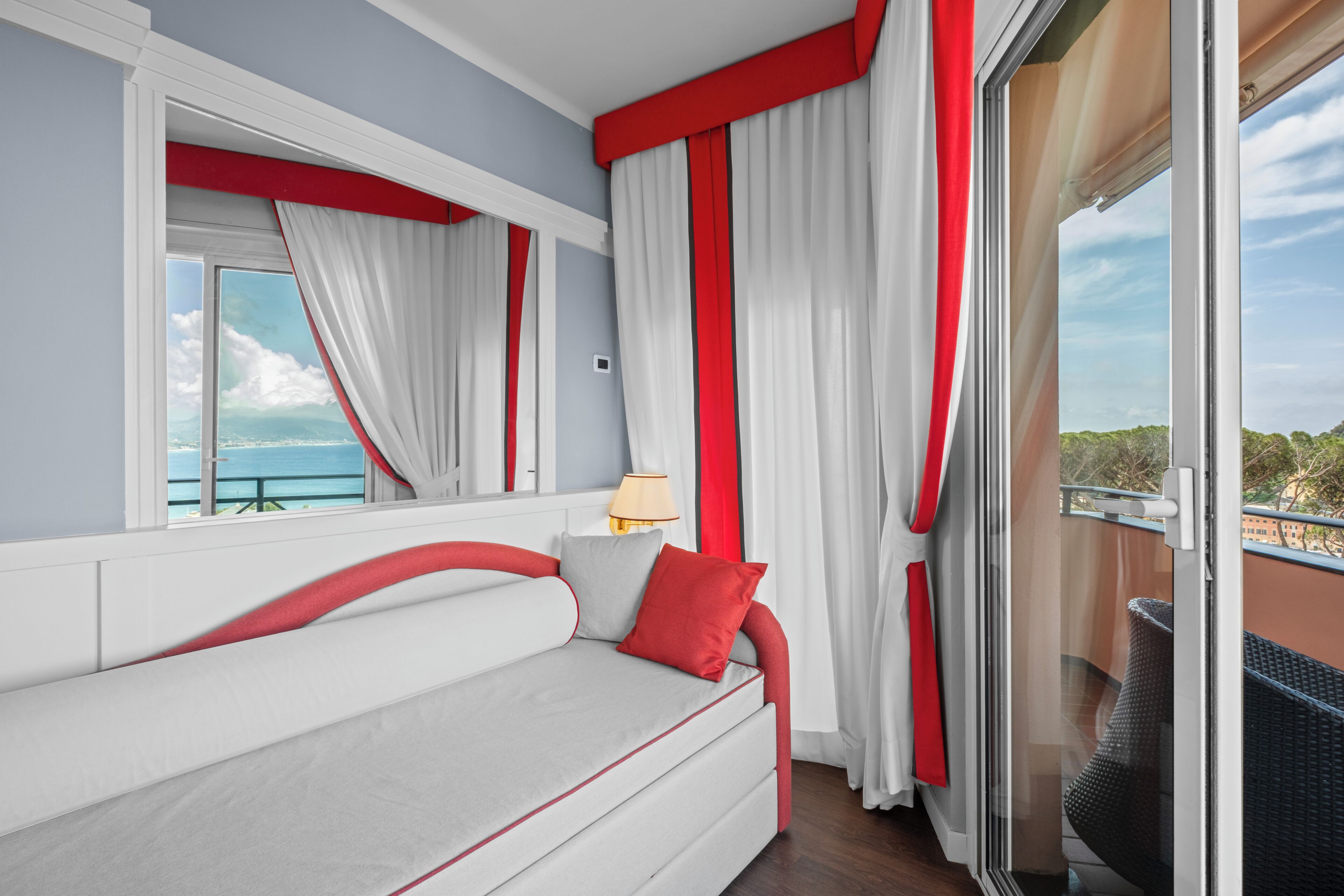 Ein Zimmer mit einer Couch, einem fenster mit Vorhängen, einer Lampe und Blick ins Freie.