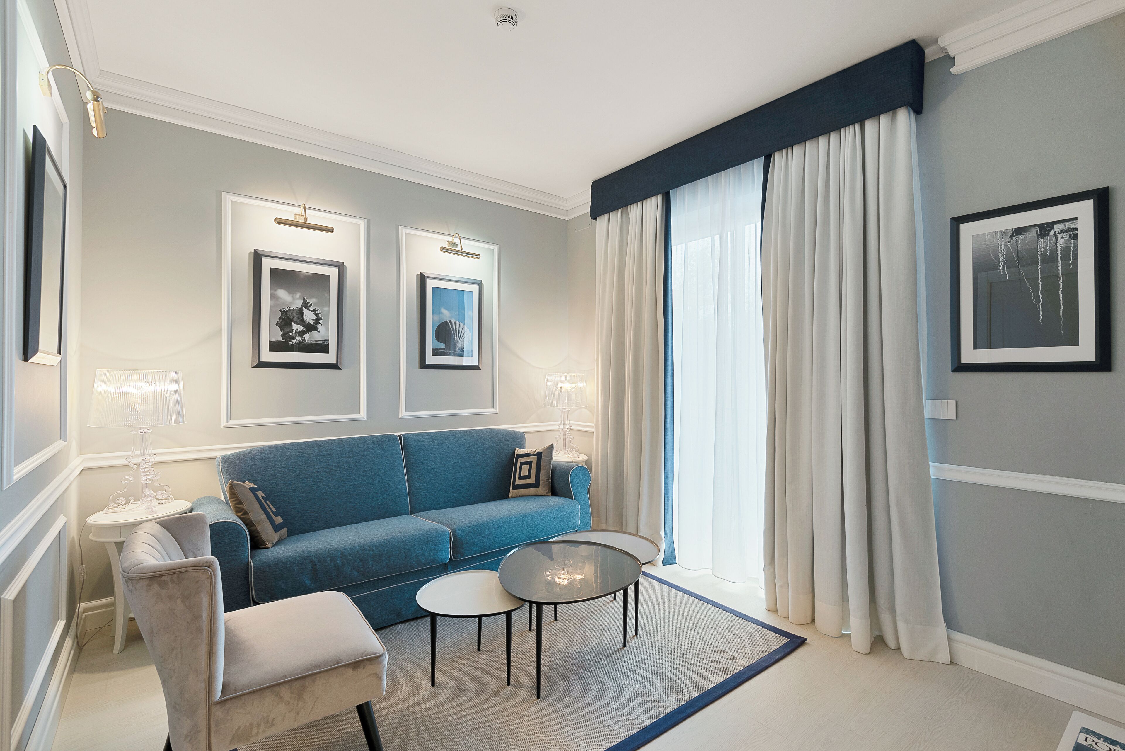 A modern living room with a blue sofa, two framed pictures, a small table, and a large window with curtains.