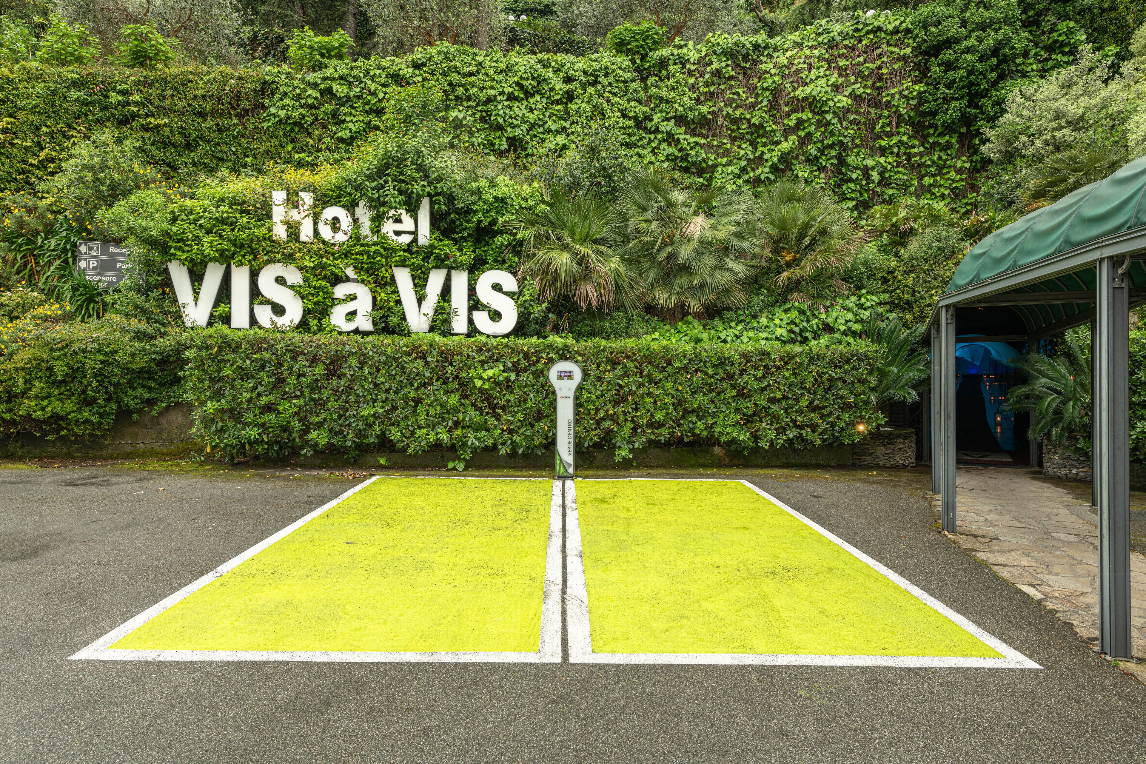 Un court de tennis avec une pancarte indiquant « Hôtel VIS a VIS » et, au fond, un panneau de signalisation indiquant un parking.