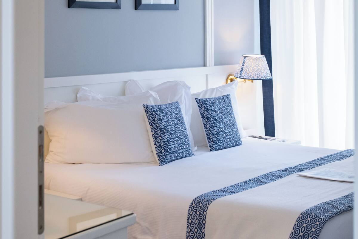 A neatly made bed with white and blue patterned bedding, a bedside lamp, and two framed pictures on the wall.