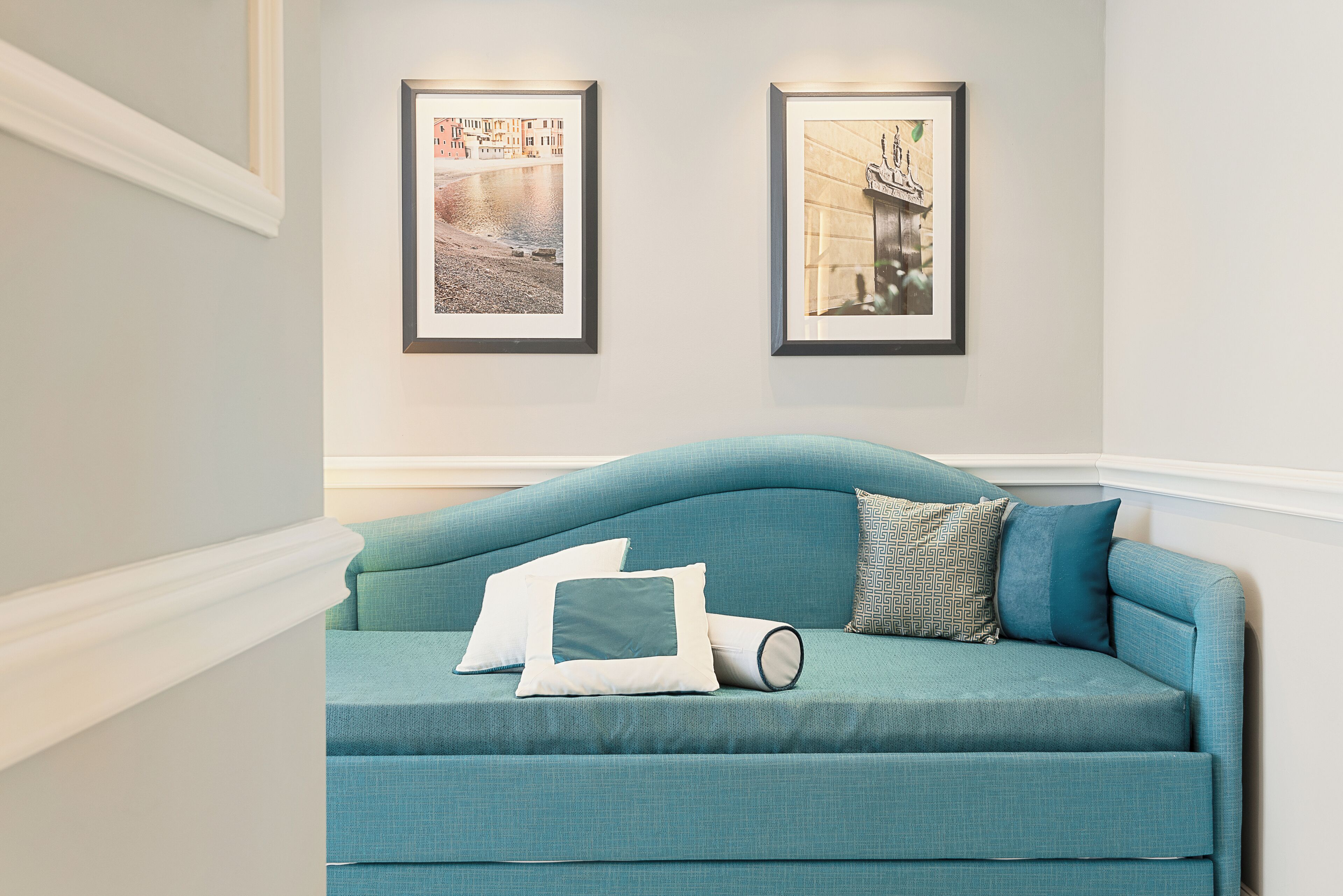 A teal sofa with pillows, a framed picture of a cityscape, and another framed picture of a statue.