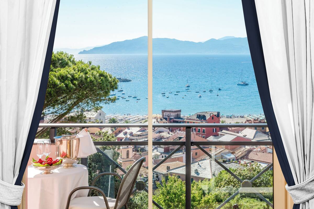 A balcony with a table set for two, overlooking a coastal town and the sea.