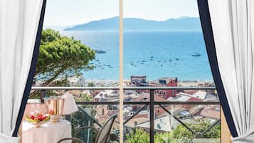 Uma varanda com mesa posta para dois, com vista para uma vila costeira e o mar.