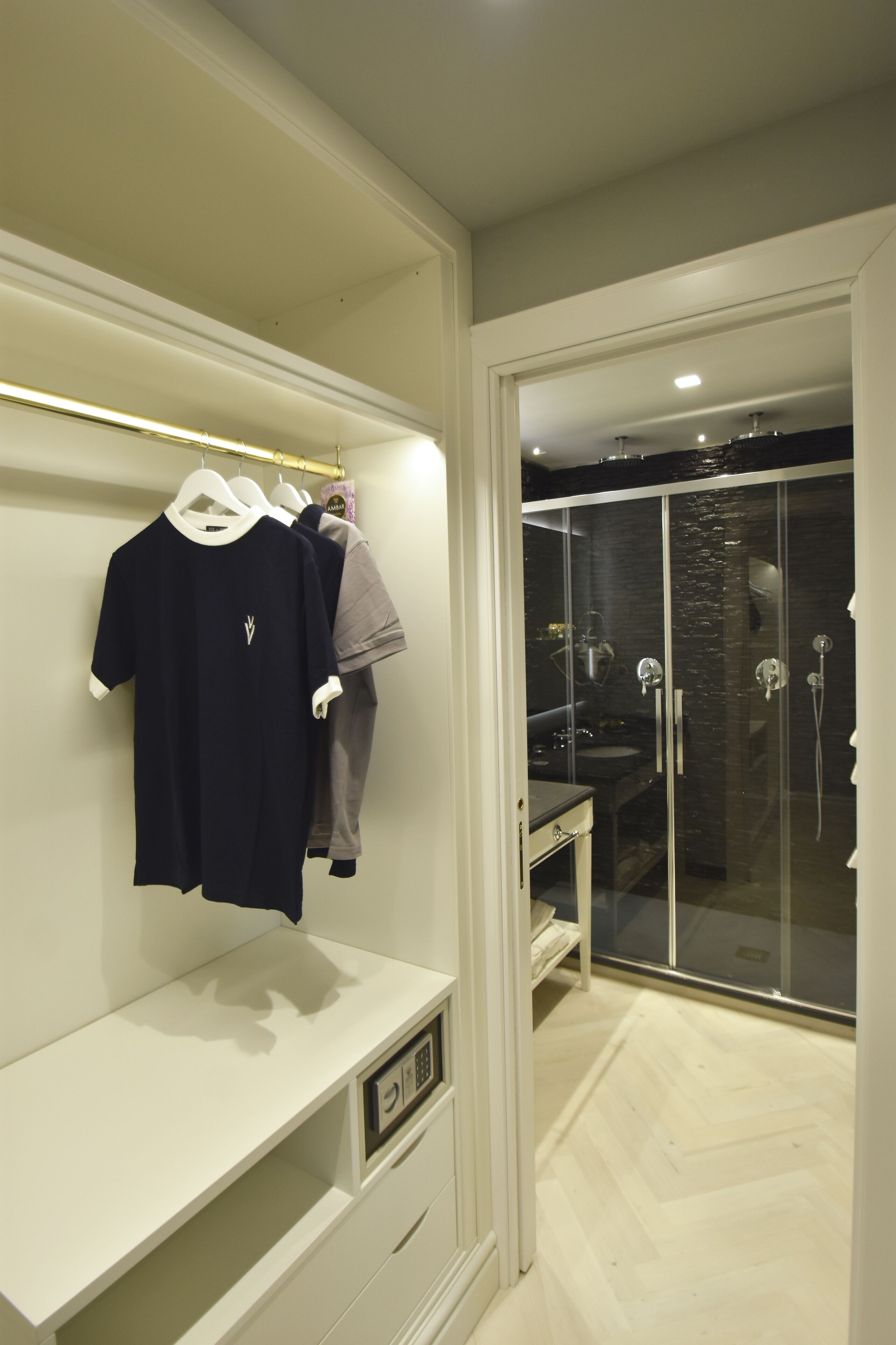 A modern bathroom with a glass shower enclosure, a vanity with a mirror, and a clothing rack with casual wear.