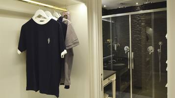 A modern bathroom with a glass shower enclosure, a vanity with a mirror, and a clothing rack with casual wear.