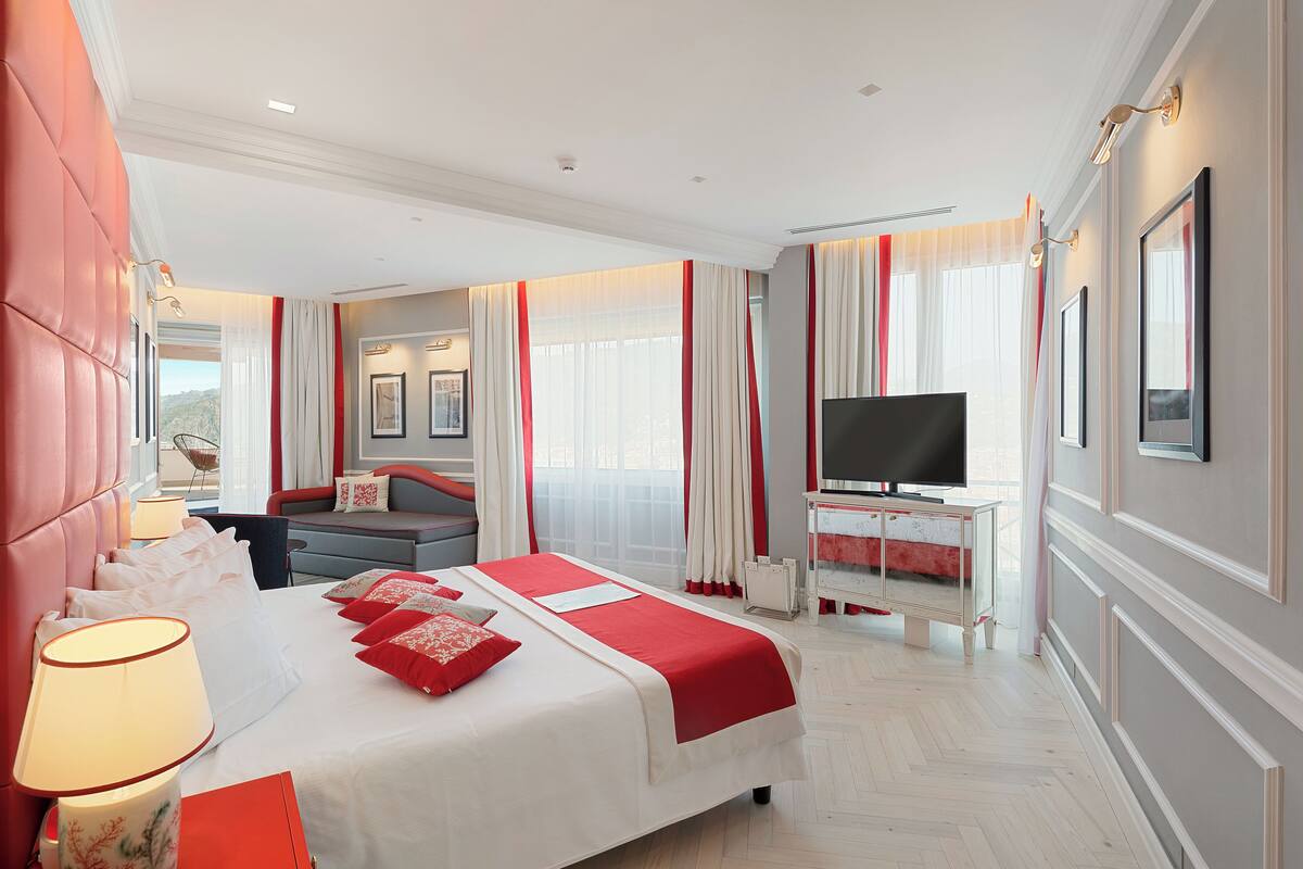 A hotel room with a large bed, a TV, a desk, and a view of the mountains.