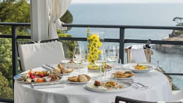 A table set for a meal with a view of the ocean, white tablecloth, and various dishes.