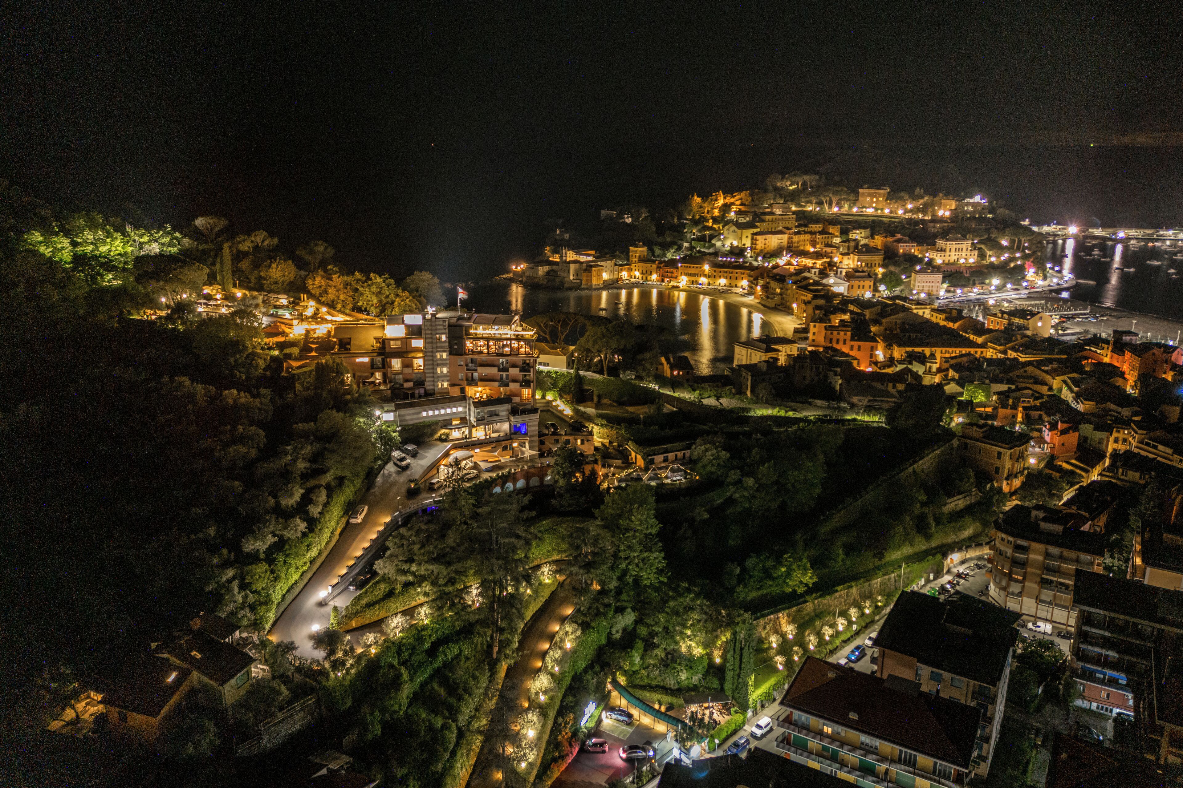 An aerial view of a historic town with buildings along a river, surrounded by greenery.