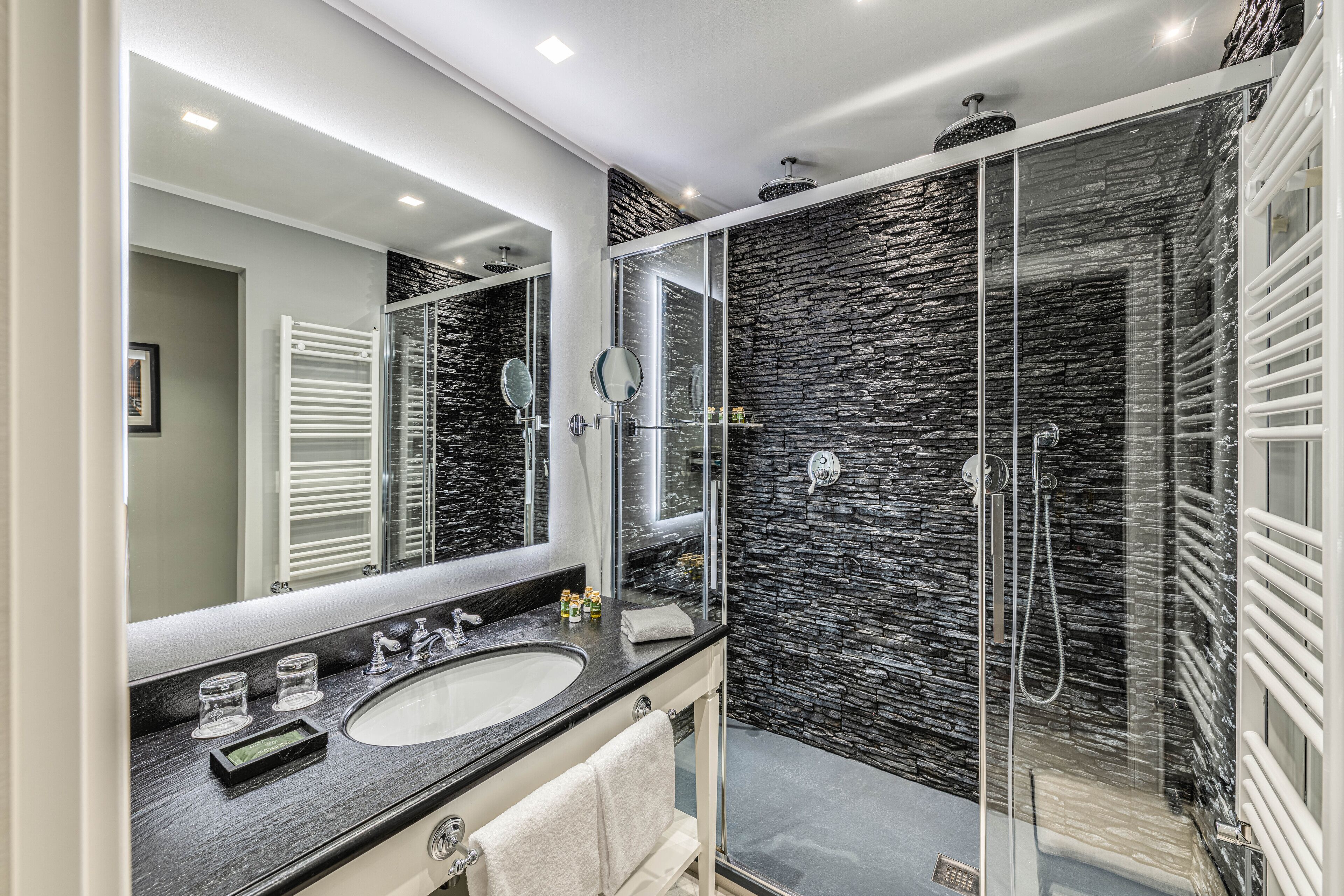 A modern bathroom with a stone wall shower, a large mirror, and a white towel.