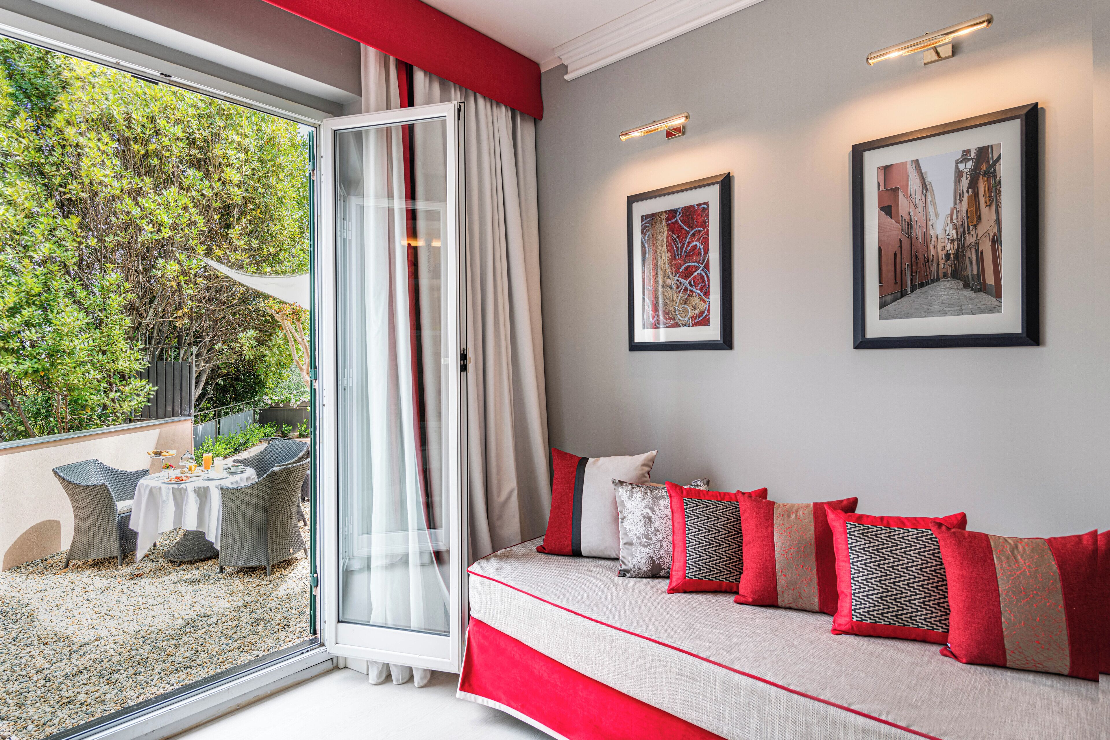 Una habitación con un ventanal grande, un sofá con cojines rojos y dos cuadros en la pared.