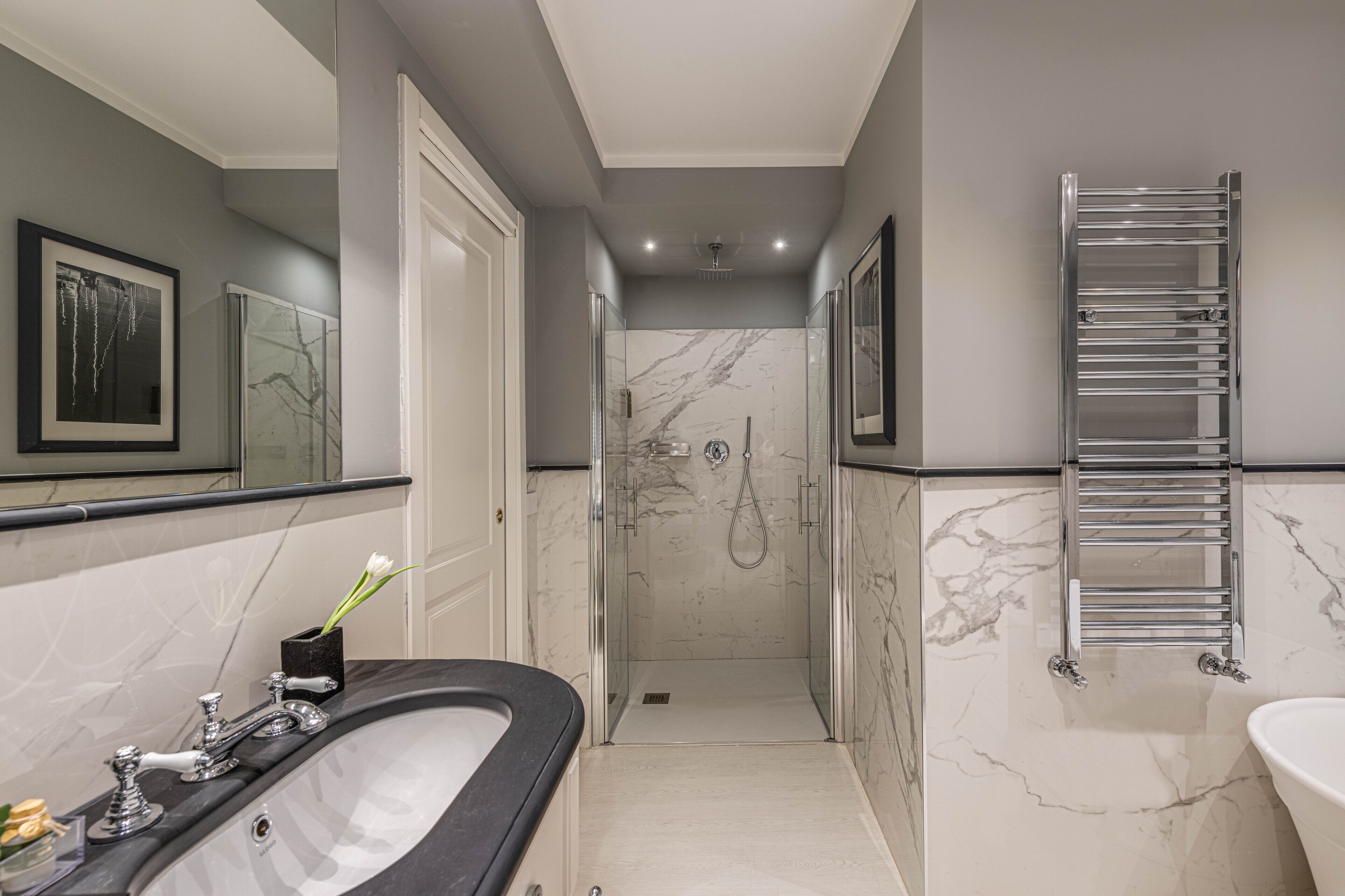 A modern bathroom with a large bathtub, a glass-enclosed shower, and a marble-tiled wall.