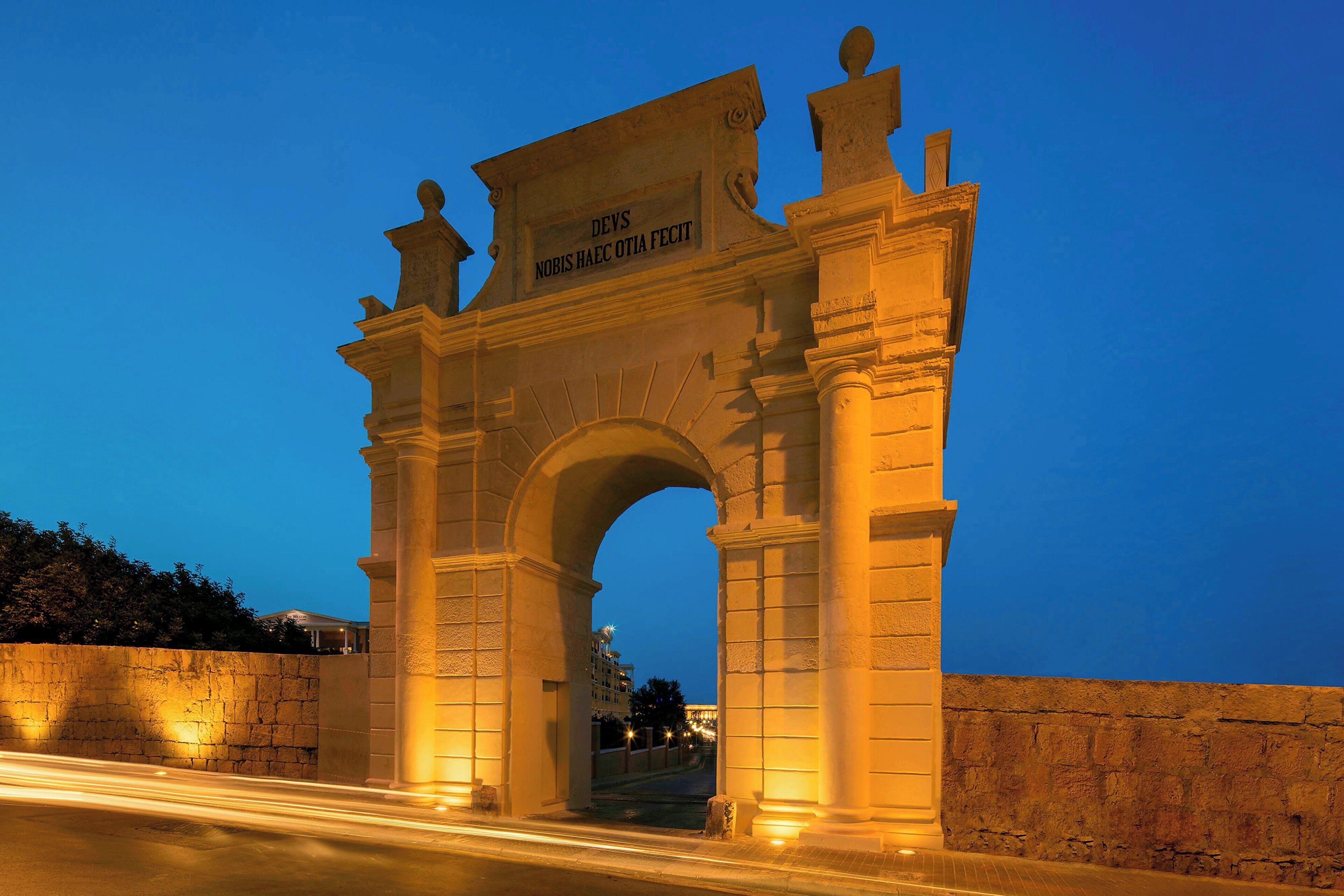 An illuminated historical archway with inscriptions, set against a twilight sky.