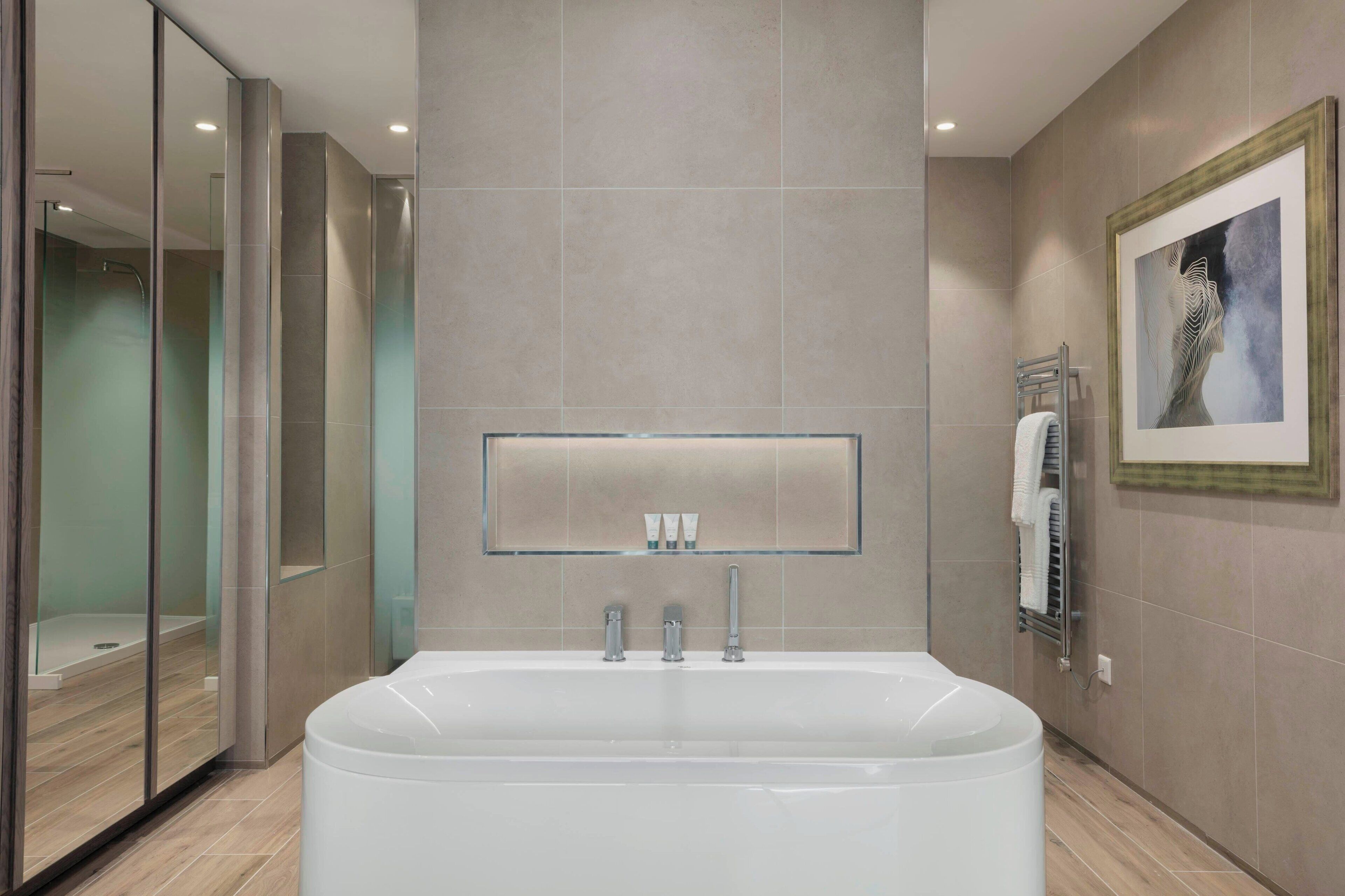 A modern bathroom with a large bathtub, a glass shower enclosure, and a framed artwork on the wall.