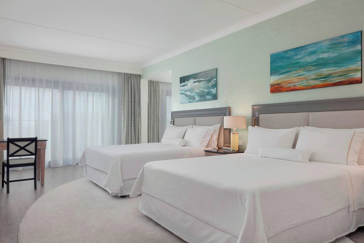 A hotel room with two beds, a desk, and a chair.