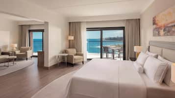 Habitación de hotel con una cama grande, dos sillones, una mesita y un balcón con vista al mar.