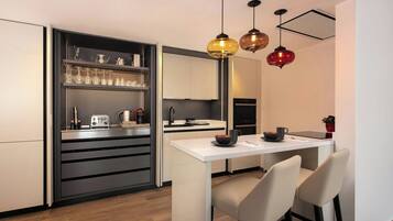 Una cocina moderna con encimera blanca, armarios negros y una estantería empotrada para vinos. Hay dos lámparas colgantes sobre la encimera.