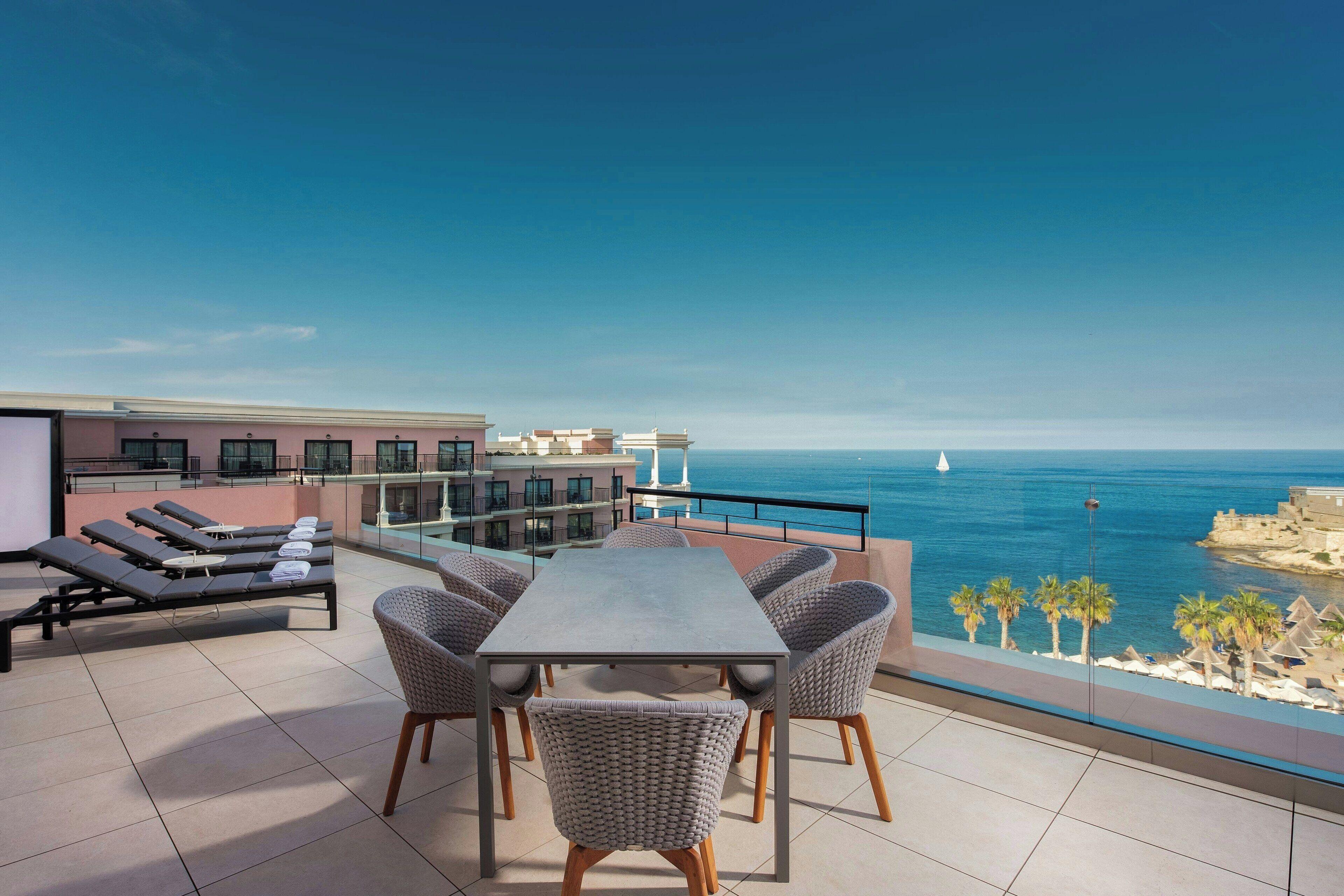A rooftop terrace with a table and chairs, a pool, and a view of the sea.