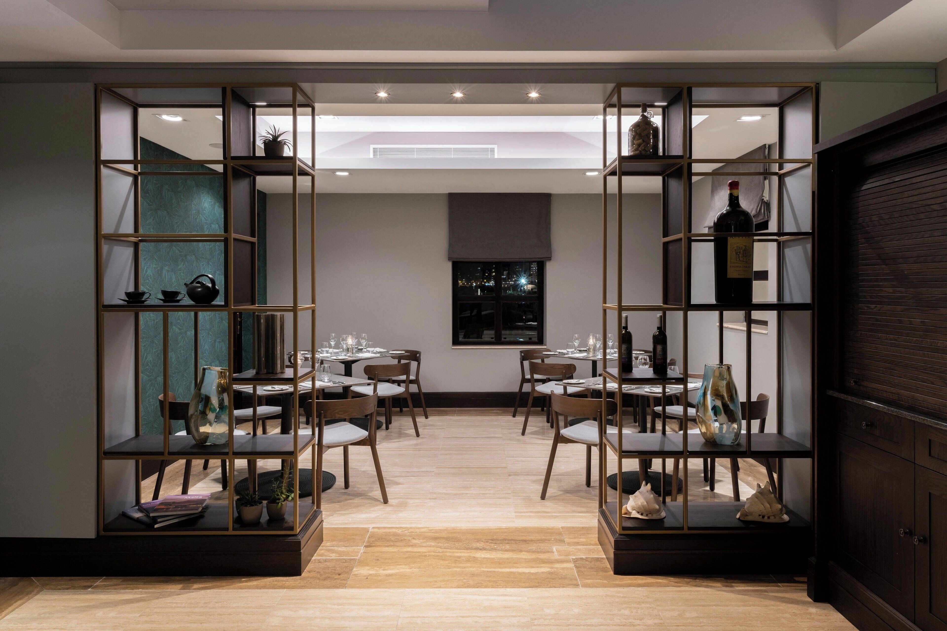 A dining area with a modern design, featuring a central table surrounded by chairs, flanked by shelving units with decorative items.