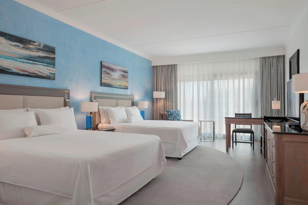 A hotel room with two beds, a desk, and a chair.