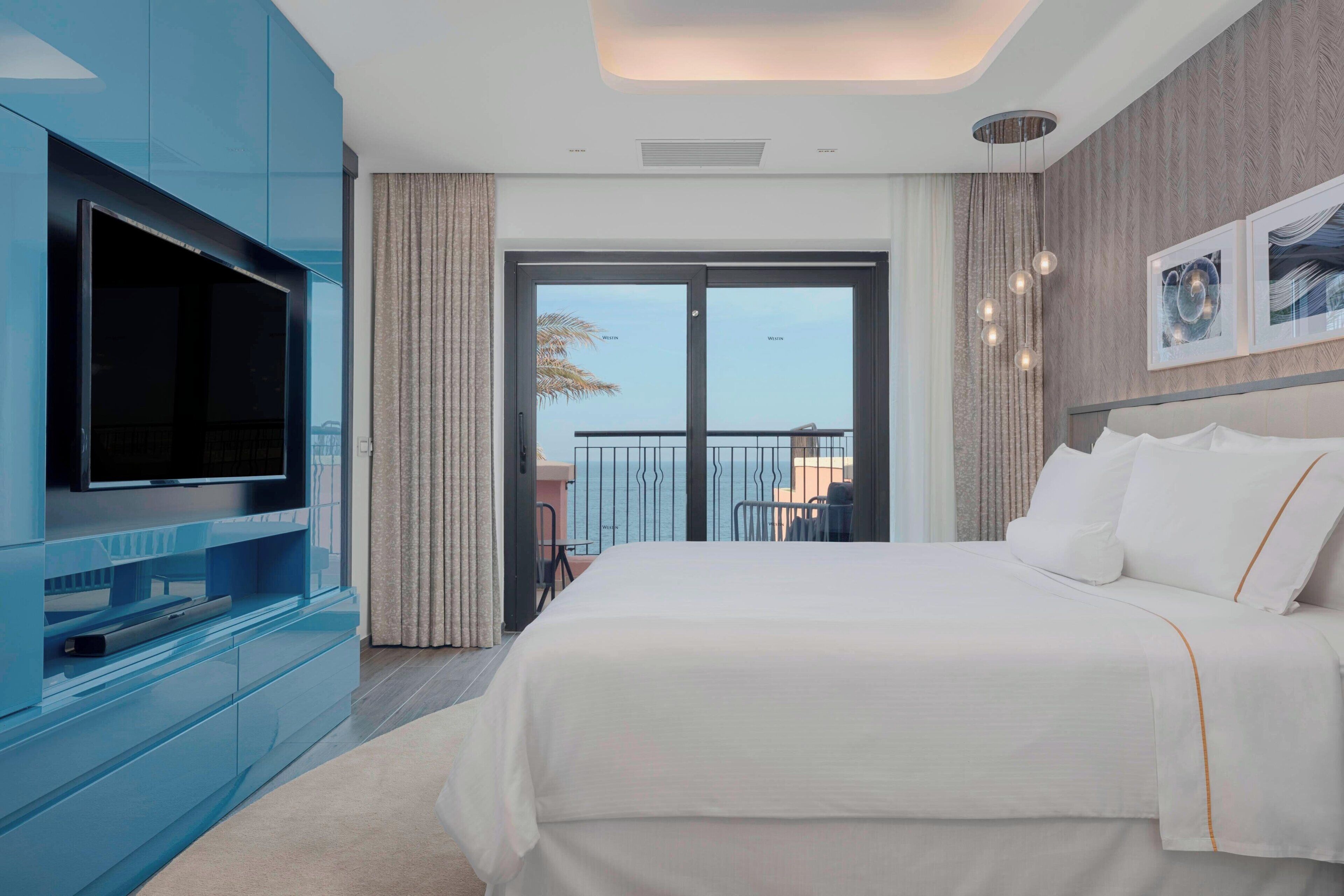 A modern hotel room with a large bed, a flat-screen TV, and a balcony with a view.