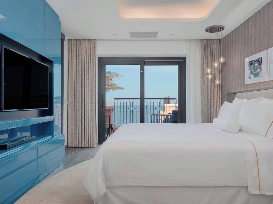 A modern hotel room with a large bed, a flat-screen TV, and a balcony with a view.