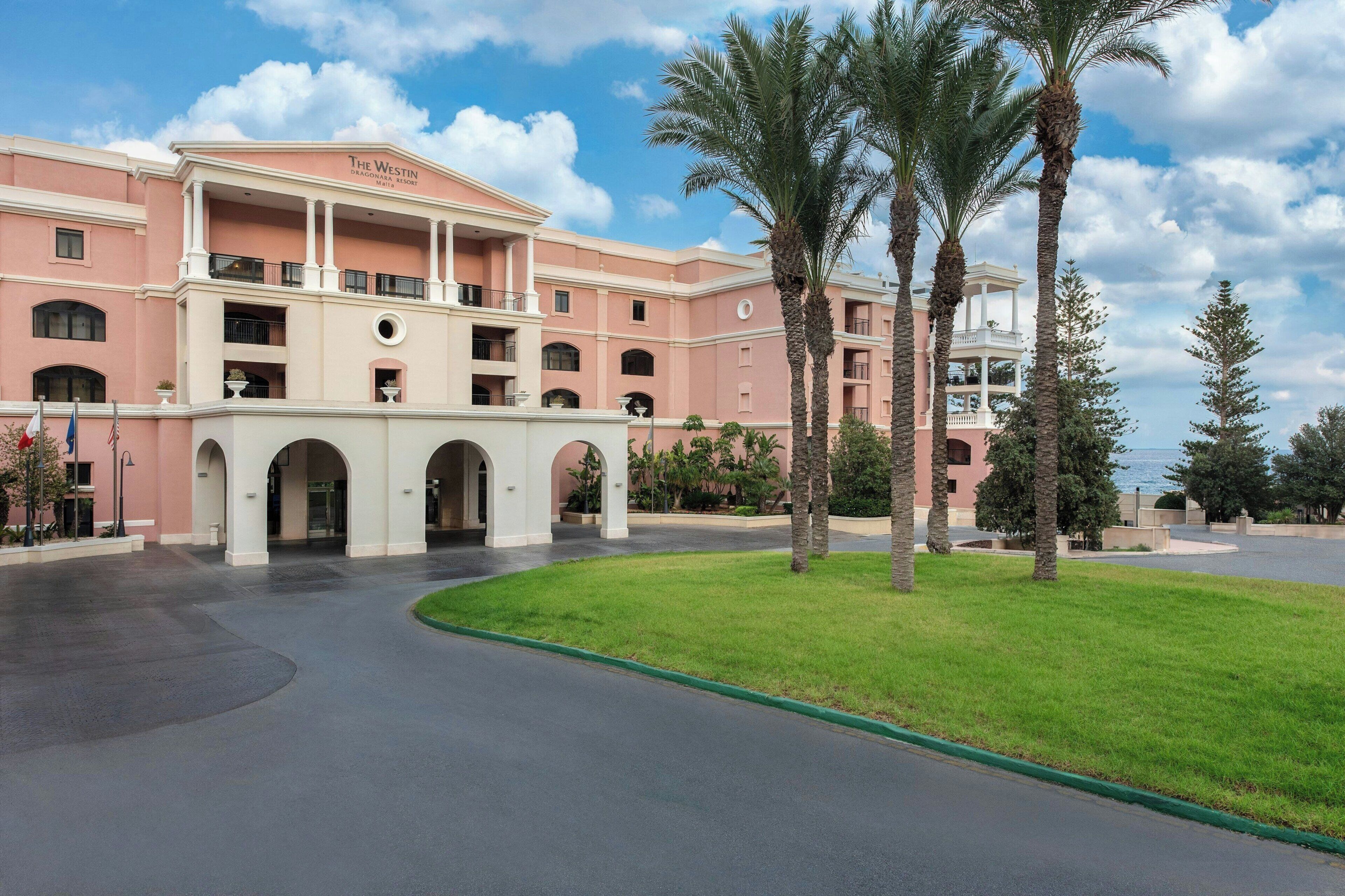 A hotel with a pink facade, multiple balconies, and palm trees.