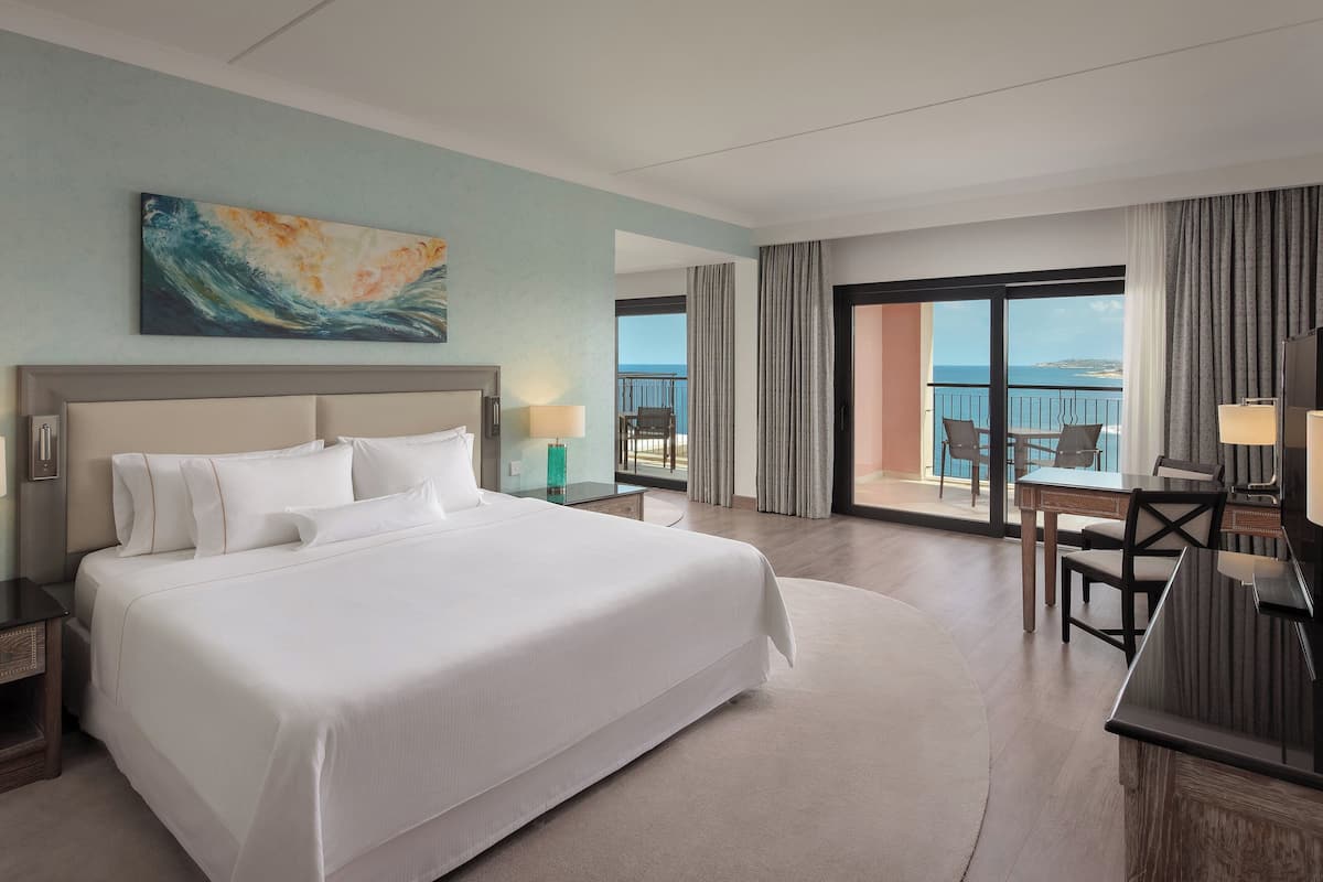 A hotel room with a large bed, a desk, and a view of the ocean.