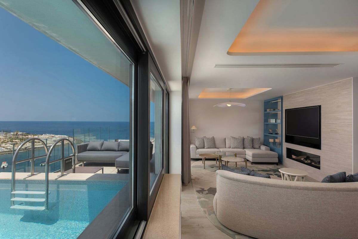 A modern living room with a pool, a sofa, a TV, and a view of the ocean.