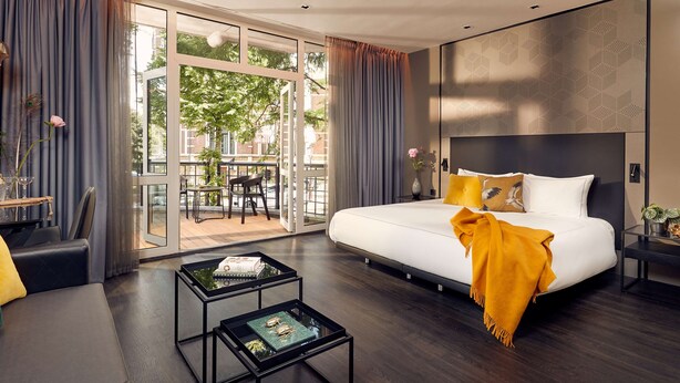 A modern hotel room with a large bed, a glass door leading to an outdoor area, and a small table with decorative items.