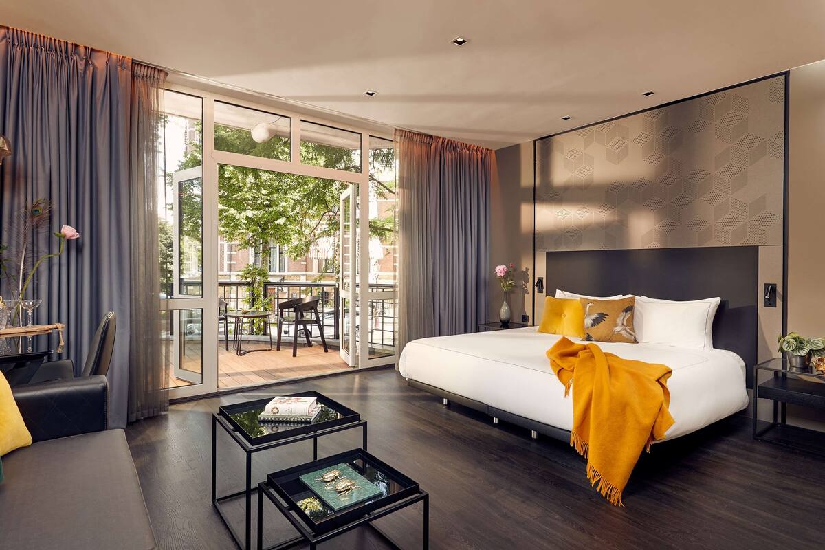 Una habitación de hotel moderna con una cama grande, una puerta de vidrio que da a un espacio exterior y una pequeña mesa con objetos decorativos.