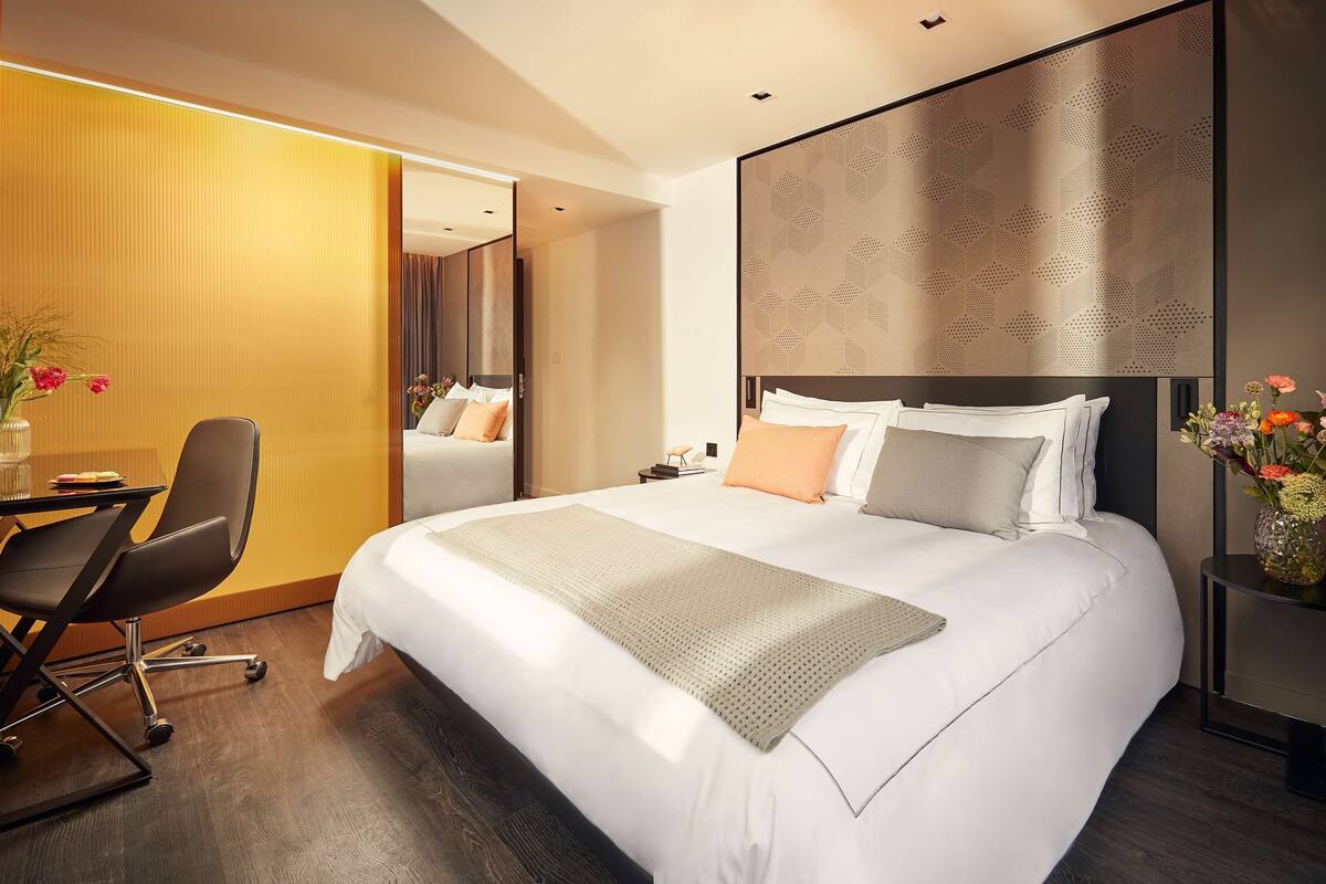 Una habitación de hotel moderna con una cama grande, un escritorio con silla y una mesita de noche.
