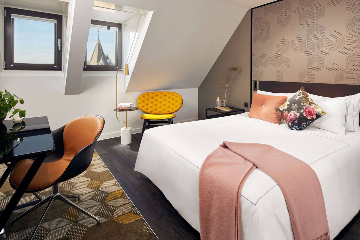 Habitación de hotel con una cama grande, un escritorio, una silla y una ventana con vistas a un edificio.