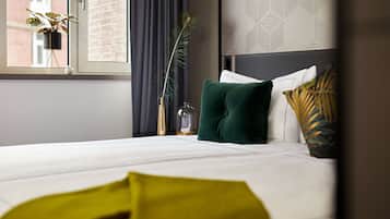A neatly made bed with white linens, a green pillow, and a decorative plant in a black pot on the windowsill.