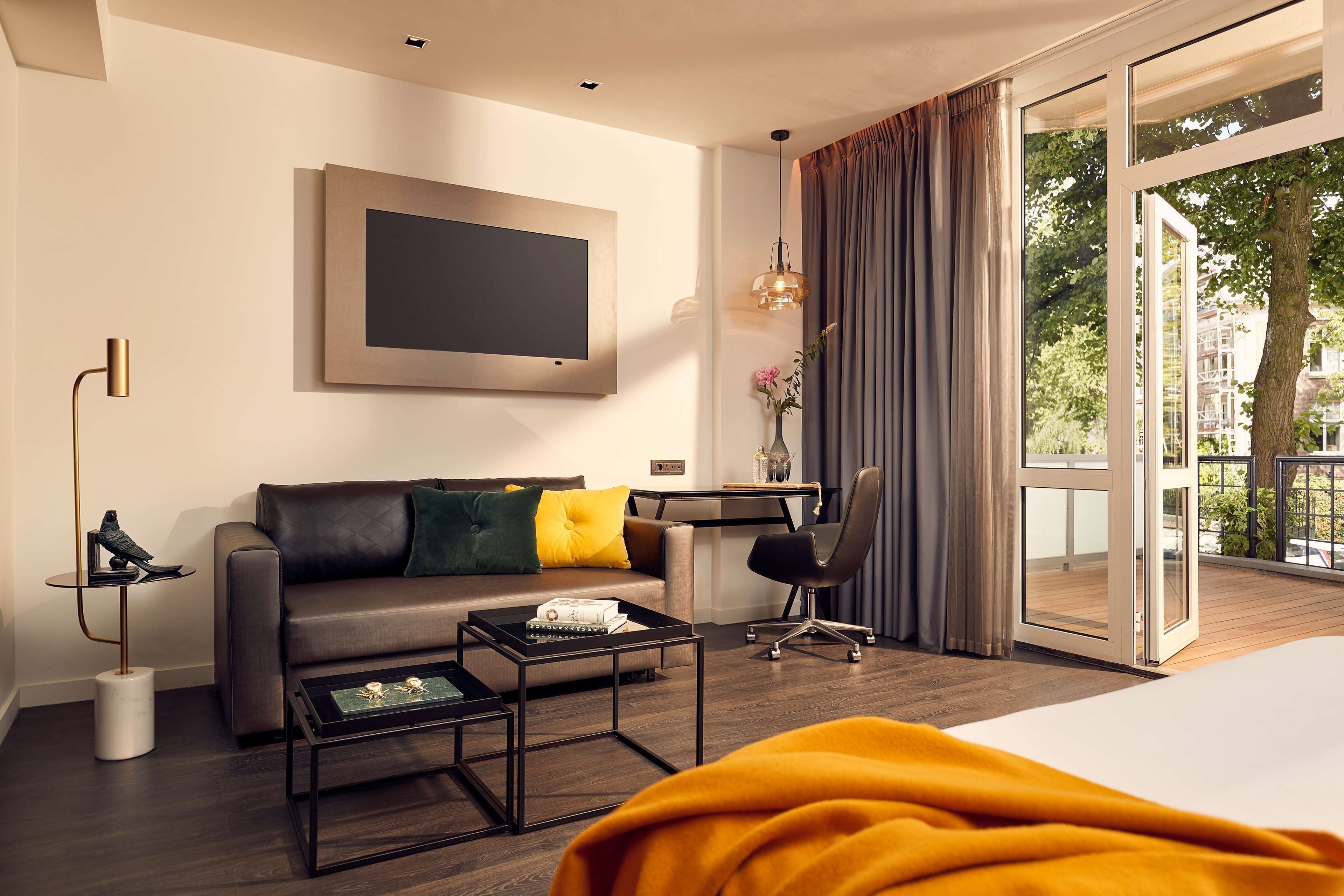 Een moderne hotelkamer met een bank, een bureau, een stoel, een televisie en een groot raam met gordijnen.