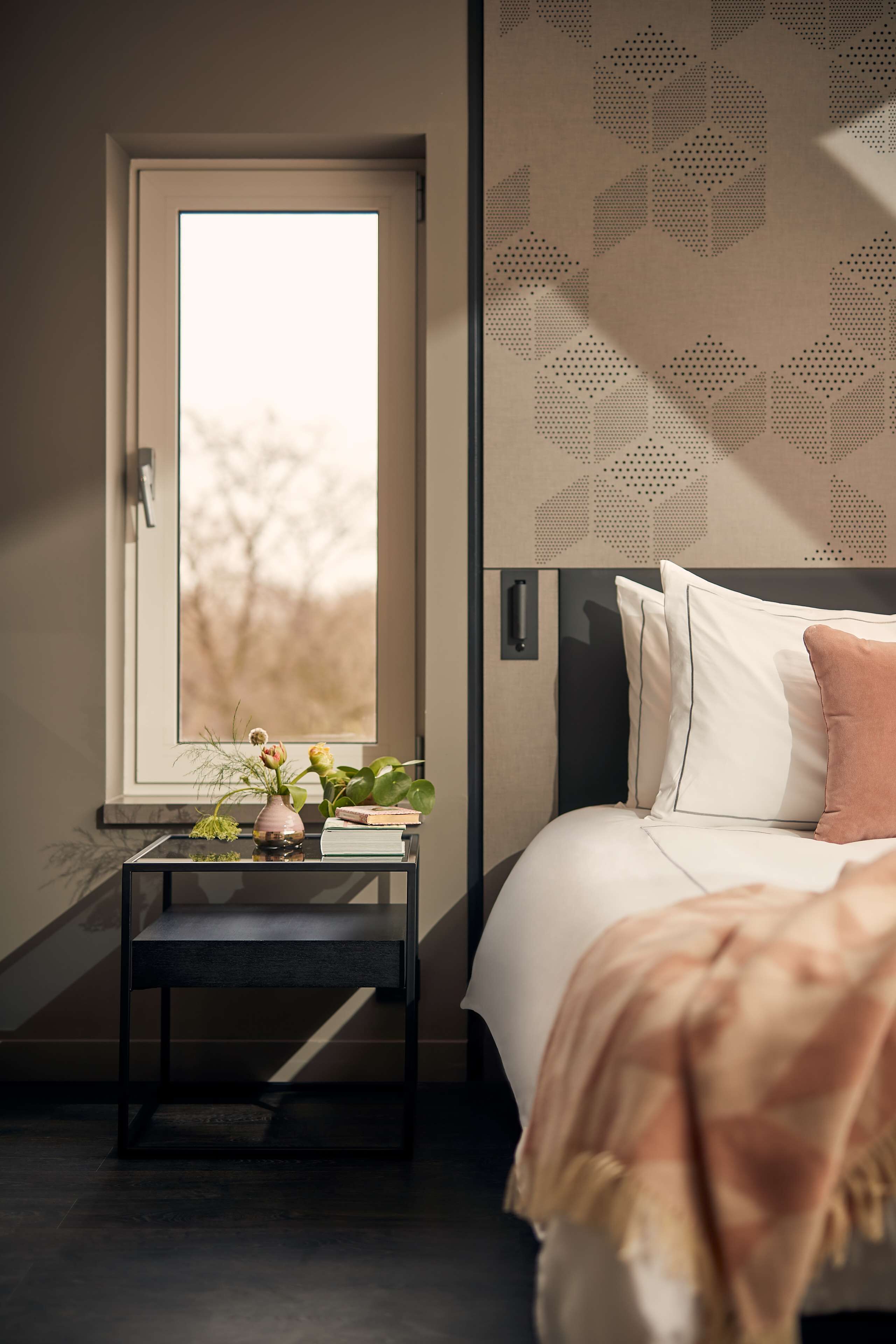 Un dormitorio con cama, mesita de noche y ventana con vistas a árboles.
