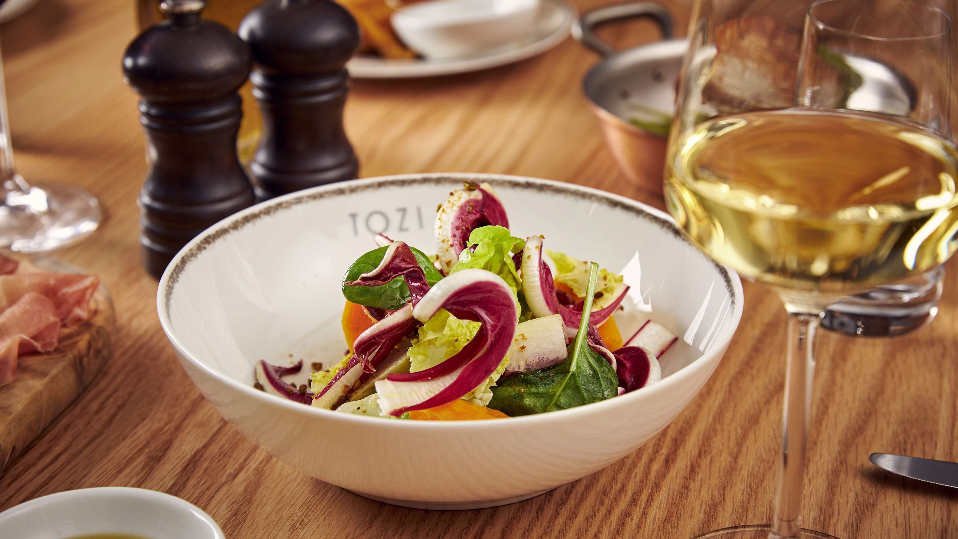 Un saladier rempli de salade composée, avec divers légumes, et un verre de vin blanc, le tout posé sur une table en bois.