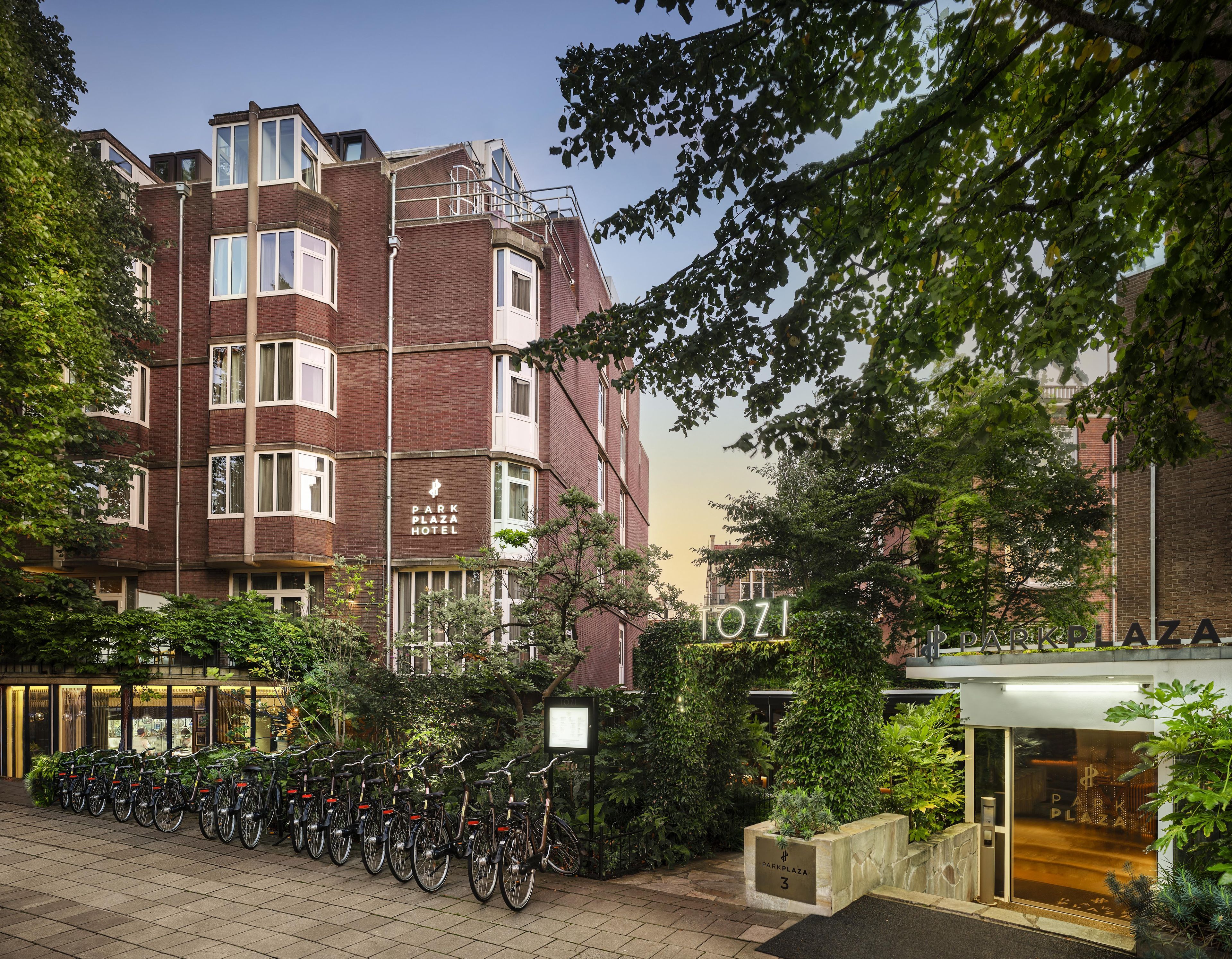Un hôtel à la façade en briques, dot é de nombreuses fenêtres et d’une enseigne indiquant « Park Plaza Hotel ». On peut voir des vélos garés à l’extérieur et de la verdure tout autour.