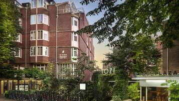 Een hotel met een gevel van baksteen, meerdere ramen en een bord met de tekst Park Plaza Hotel. Fietsen staan er geparkeerd en er is groen te zien.