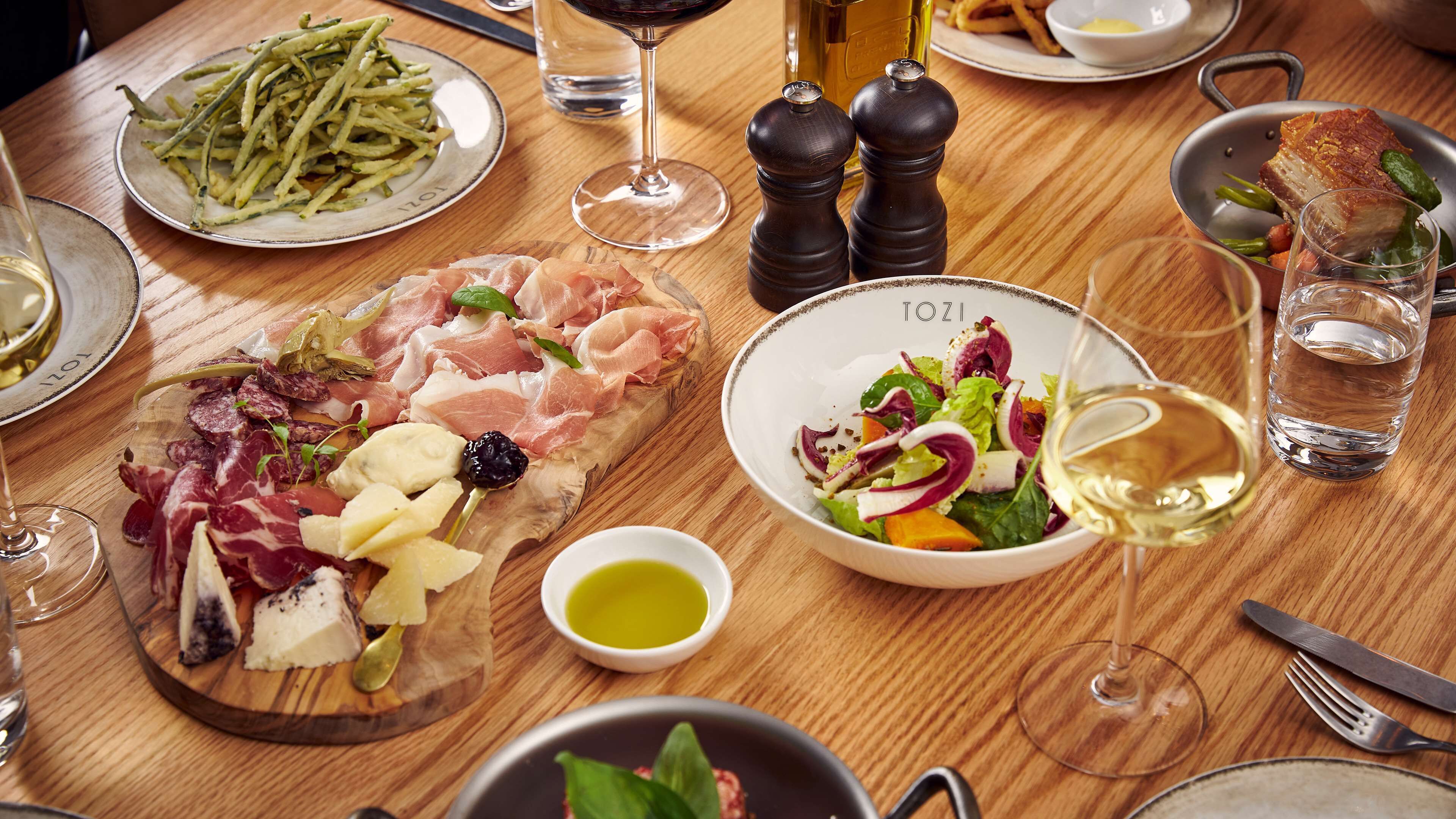 A wooden table with a variety of food items including charcuterie, a salad, and a plate of fries.